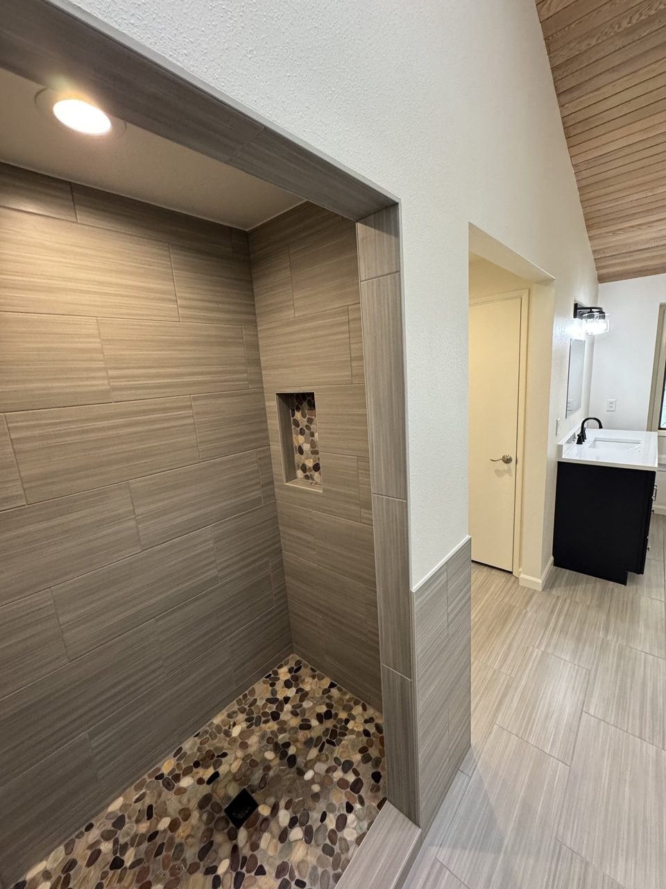 Walk-in shower with horizontal tile, pebble floor, and accent niche
