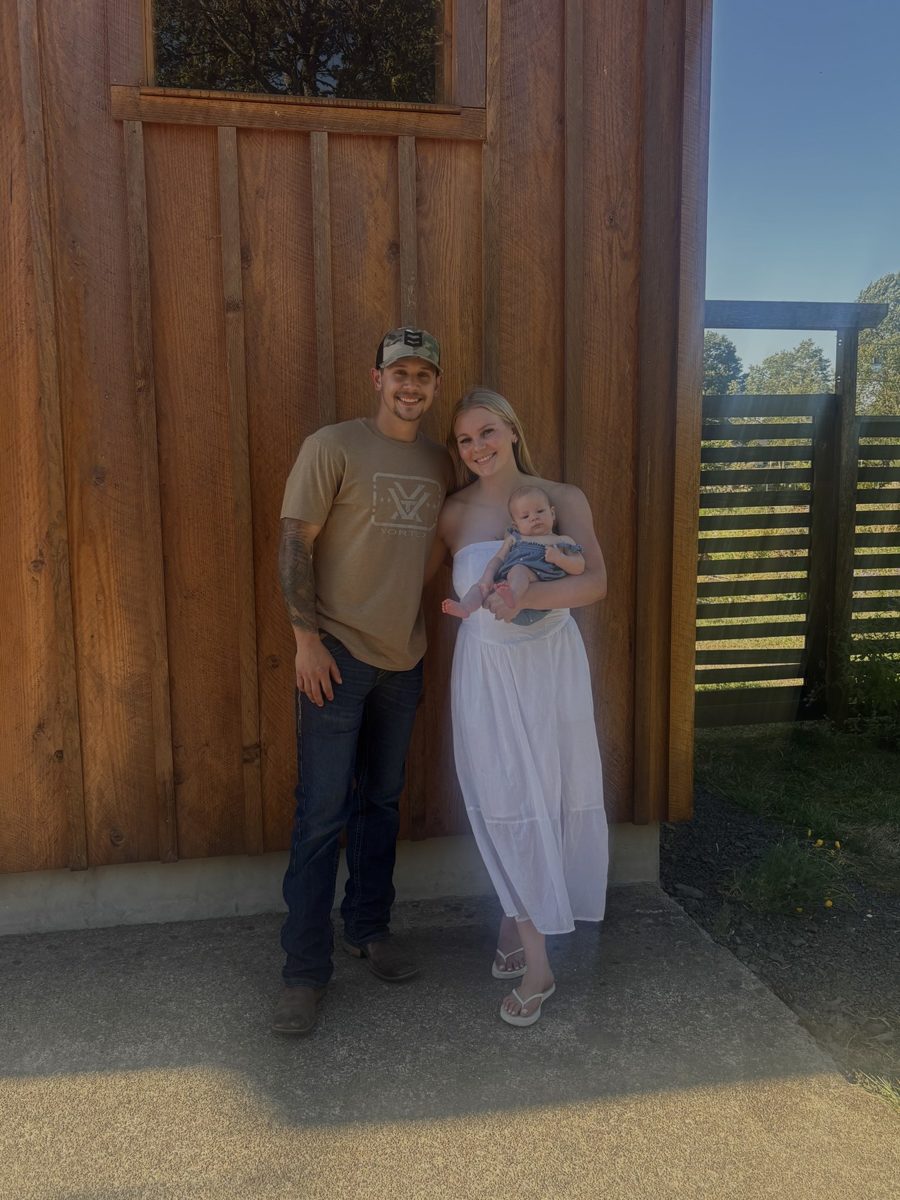 Deavin Brownson standing with his wife and daughter outside a wood-sided building