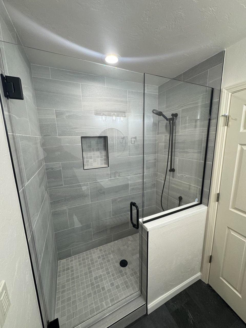 Finished gray tile shower with glass enclosure and built-in niche